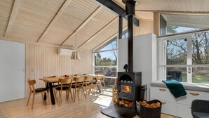 Una habitació acollidora amb sostre de fusta, una taula de menjador amb cadires, un sofà amb una manta i un foc de llenya.