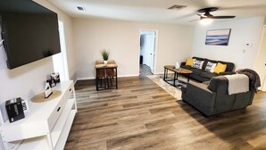 A modern living room with a flat-screen TV, a sofa with cushions, a coffee table, and a small side table with a plant. - Astor Serene Riverfront Retreat with 2 boat slips and a dock (Astor)