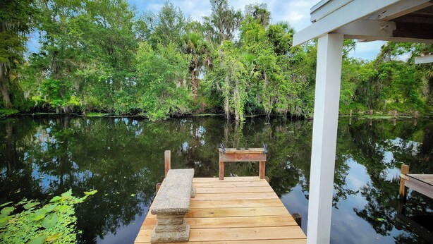 A wooden dock extending into a calm lake, surrounded by lush greenery and trees. - Astor Serene Riverfront Retreat with 2 boat slips and a dock (Astor)