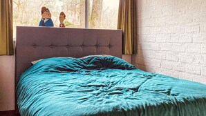 A bedroom with a tufted headboard, a teal bedspread, and a window with curtains.
