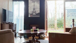 A living room with a television, a round table with decorative items, a framed picture of the Eiffel Tower, and a view of a garden through a glass door.