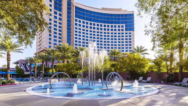 A hotel courtyard with a fountain, palm trees, and a large building in the background.