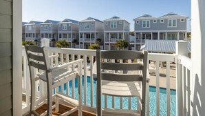 Un balcón con barandillas blancas que da a una piscina y una hilera de casas de playa con balcones.