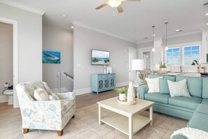 Un salon spacieux avec un canapé de couleur turquoise, un fauteuil à motifs et une table basse. On y trouve également un meuble bleu et un tableau accroché au mur.