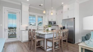 Cocina moderna con armarios blancos, una isla central con sillas, un refrigerador de acero inoxidable y vistas a través del ventanal.