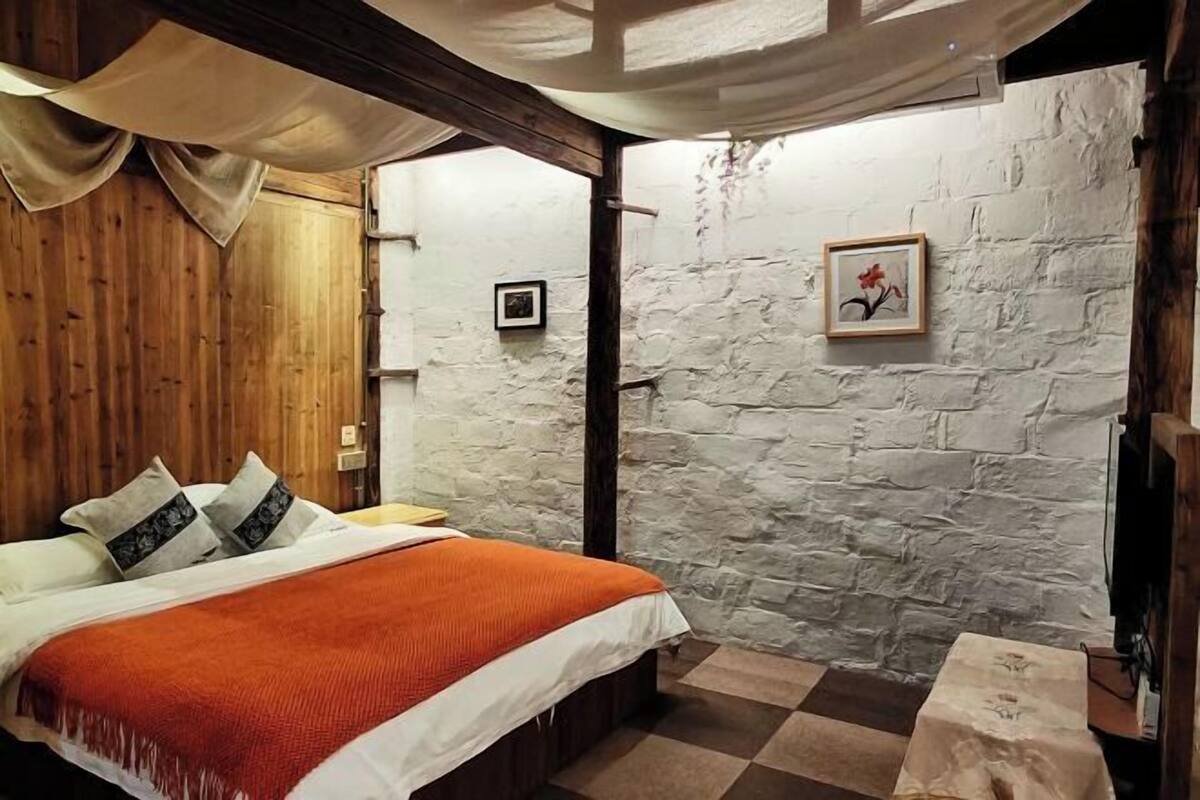 A bedroom with a bed, wooden walls, a stone wall, and a framed picture on the stone wall.
