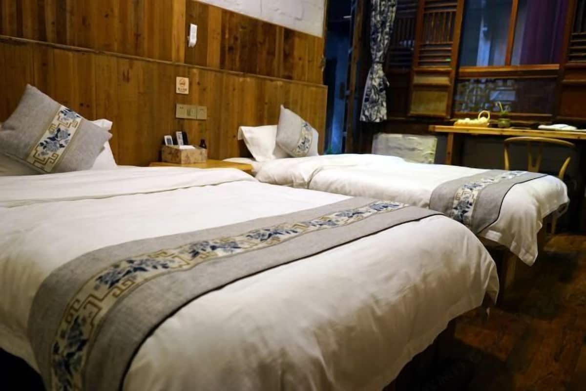 A hotel room with two beds, wooden paneling on the walls, a small table with a lamp, and a chair.