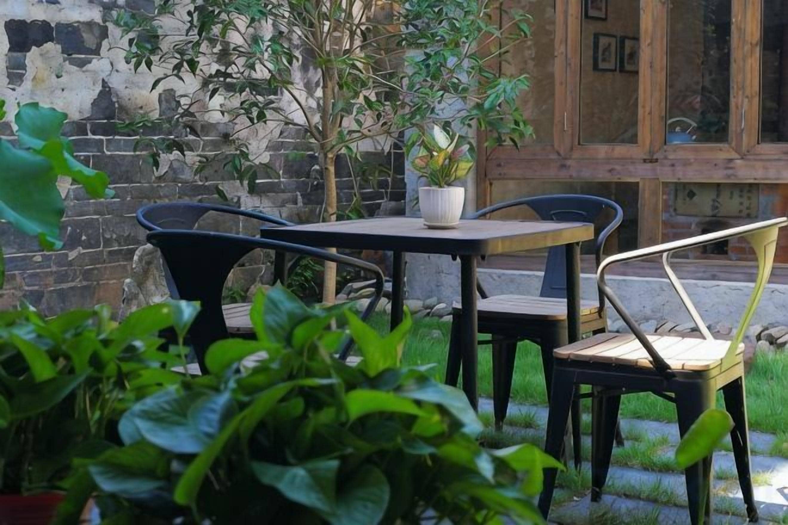 Eine Terrasse mit Tisch und Stühlen, einem Blumentopf und einer Ziegelwand.