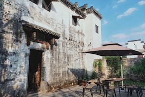 A rustic building with a tiled patio, outdoor seating, and a large umbrella providing shade. - Yanshe Inn (Huangshan City)