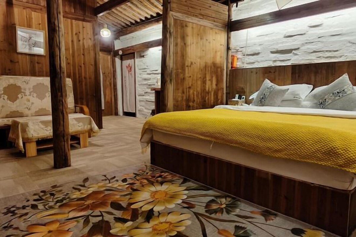 A wooden room with a bed, a chair, and a floral-patterned carpet.