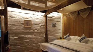 Un dormitorio acogedor con pared de piedra, vigas de madera en el techo y una cama con ropa de cama blanca.