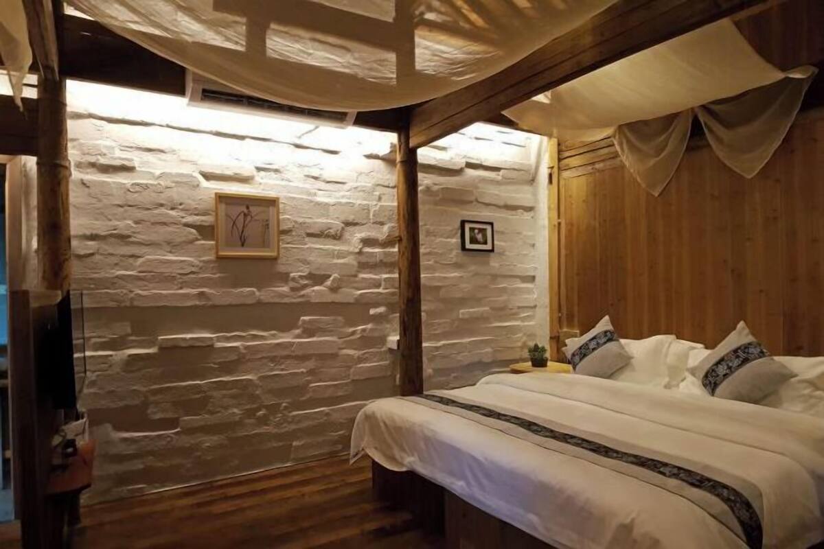 A cozy bedroom with a stone wall, wooden ceiling beams, and a bed with white bedding.