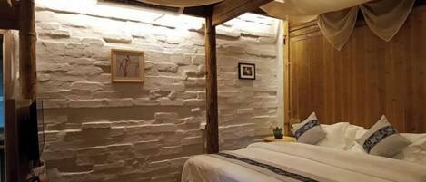 Une chambre confortable avec un mur en pierre, des poutres apparentes en bois au plafond et un lit recouvert de linge de lit blanc.