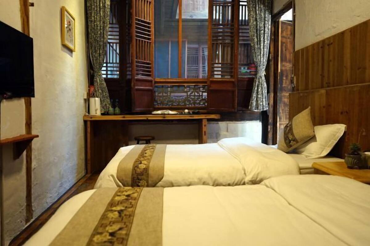 A traditional room with two beds, a wooden desk, and a window with wooden shutters.