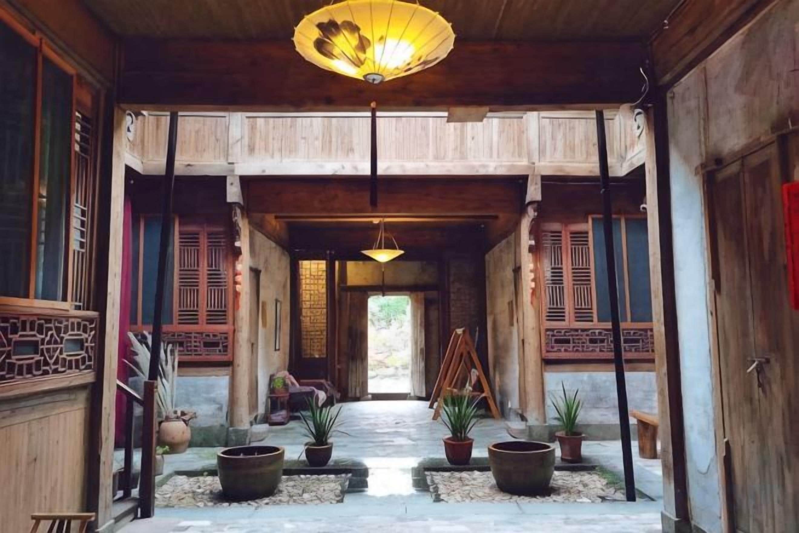 Un couloir traditionnel en bois, agrémenté d’un luminaire suspendu, de plantes en pot et d’une porte en bois au bout.