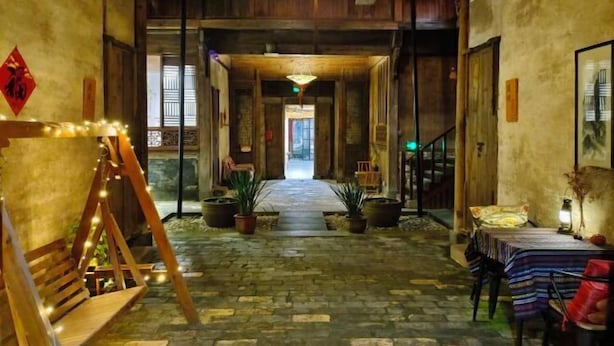 Un pasillo con suelo de madera, plantas en macetas, un columpio y una mesa con un farol.