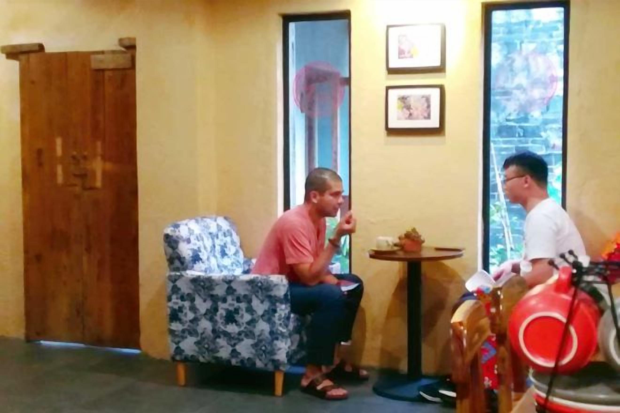 A room with a wooden door, a patterned armchair, a small round table, and a red bicycle.