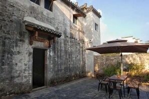 A courtyard with stone flooring, a table with chairs, and a large umbrella providing shade.