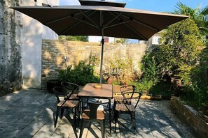 An outdoor patio with a table and chairs under a large umbrella, surrounded by stone walls and greenery. - Yanshe Inn (Huangshan City)