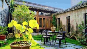 Un patio tradicional con un sendero de piedra, una mesa de madera con sillas y plantas en macetas.