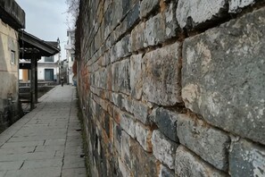 Un stretto sentiero in pietra costeggiato da un muro di pietra antico, che conduce a un edificio con un portico.