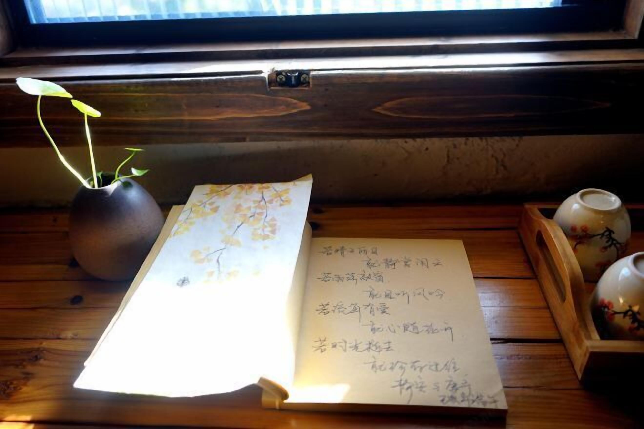 A wooden table with a vase of green plants, a book with handwritten notes, and a teapot.
