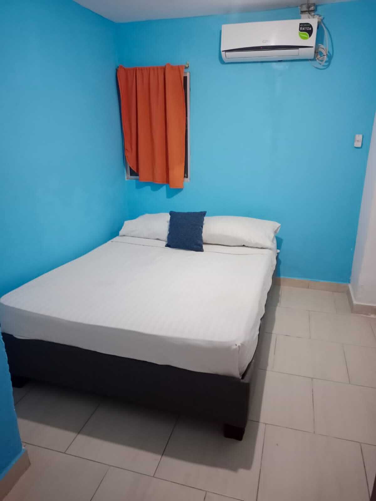 Una habitación con cama, aire acondicionado y ventana con cortinas naranjas.