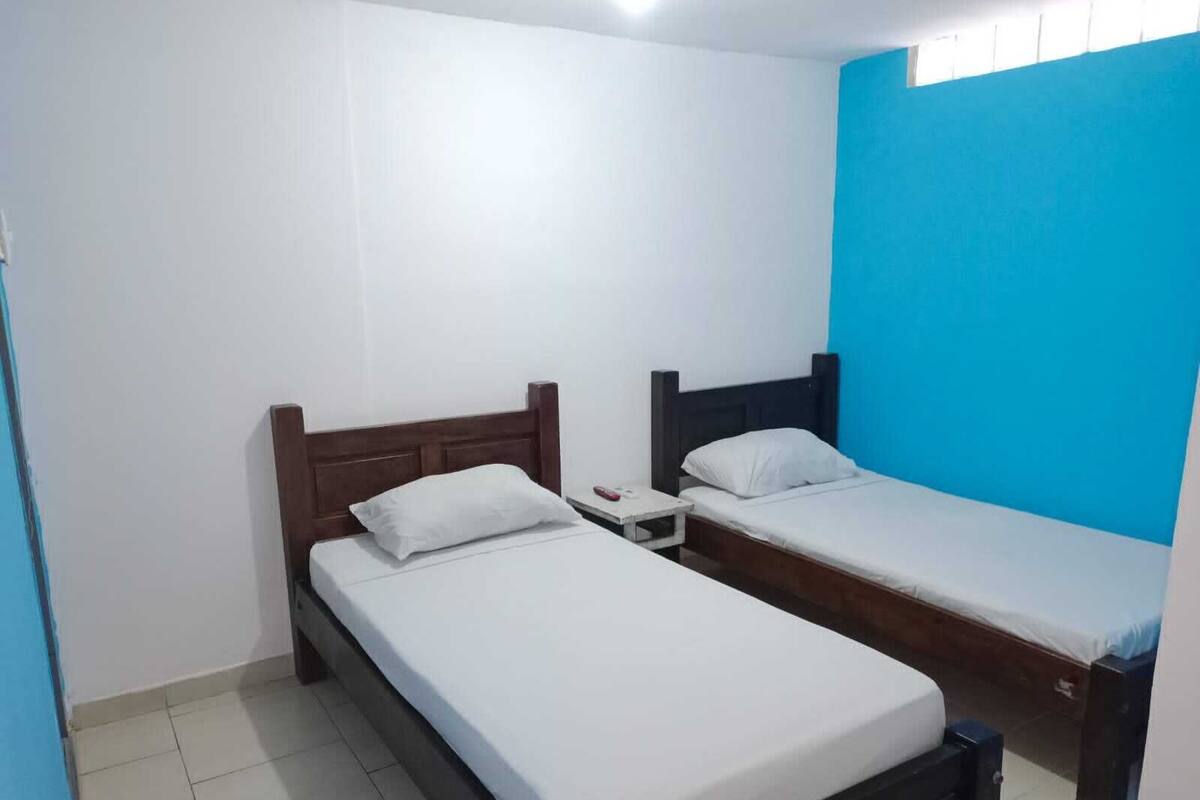 Quarto pequeno e limpo, com duas camas de solteiro, uma mesa de cabeceira e uma parede azul.