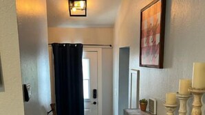 En hall med en träbänk, en dörr med en gardin och en väggmonterad lampa.