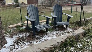 Två Adirondack-stolar i ett inhägnat utomhusområde, med snö på marken.