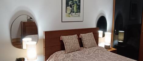 En snyggt bäddad säng med ett mönstrat överkast, två sänglampor och ett inramat konstverk ovanför sängen.