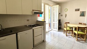 A compact kitchen with a stove, sink, and white cabinets. There's a dining area with a table and chairs. - M341 - Marcelli, Three-room apartment with garden close to the sea (Marcelli)