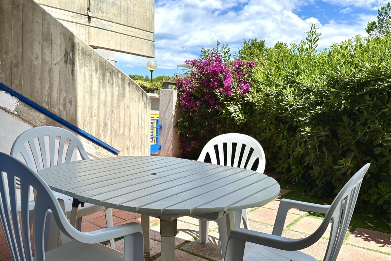A patio with a round table and four chairs, surrounded by greenery and a concrete wall.