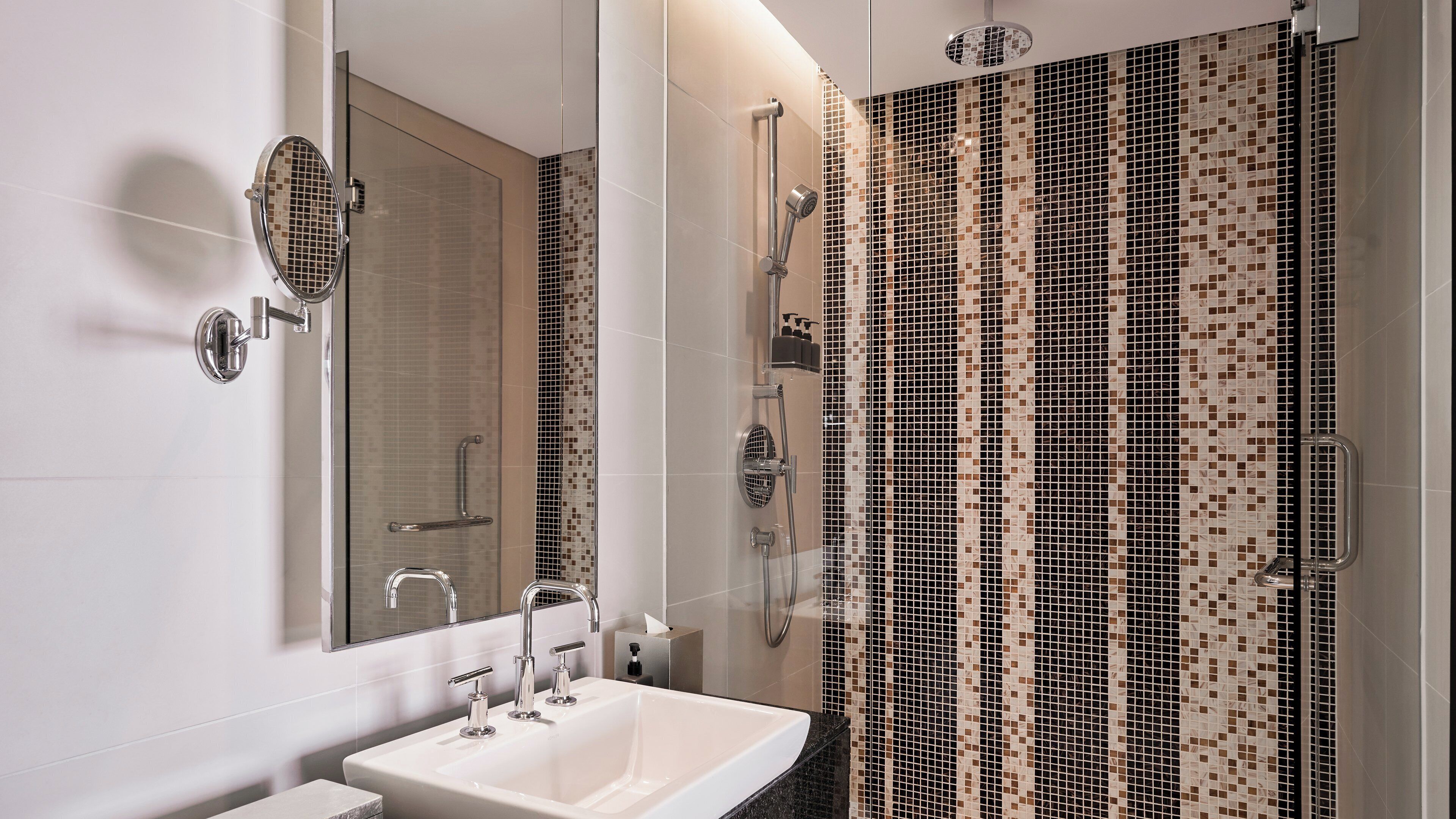 A modern bathroom with a large mirror, a white sink, and a shower with mosaic tile walls.