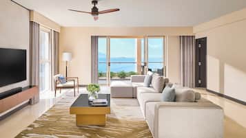 A modern living room with a flat-screen TV, a sofa, a coffee table, and a view of the sea through large windows.