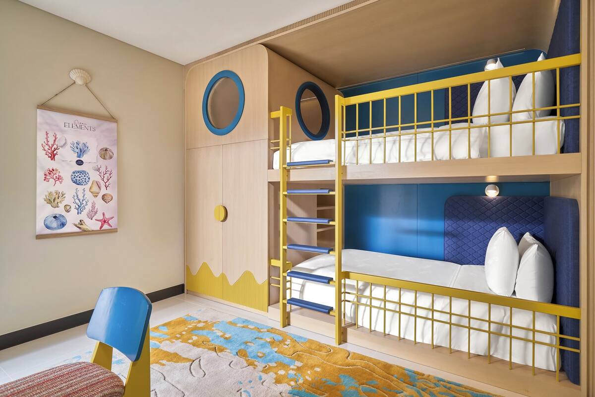 Une chambre avec un lit superposé aux couleurs bleu et jaune, une petite chaise et une affiche accrochée au mur.