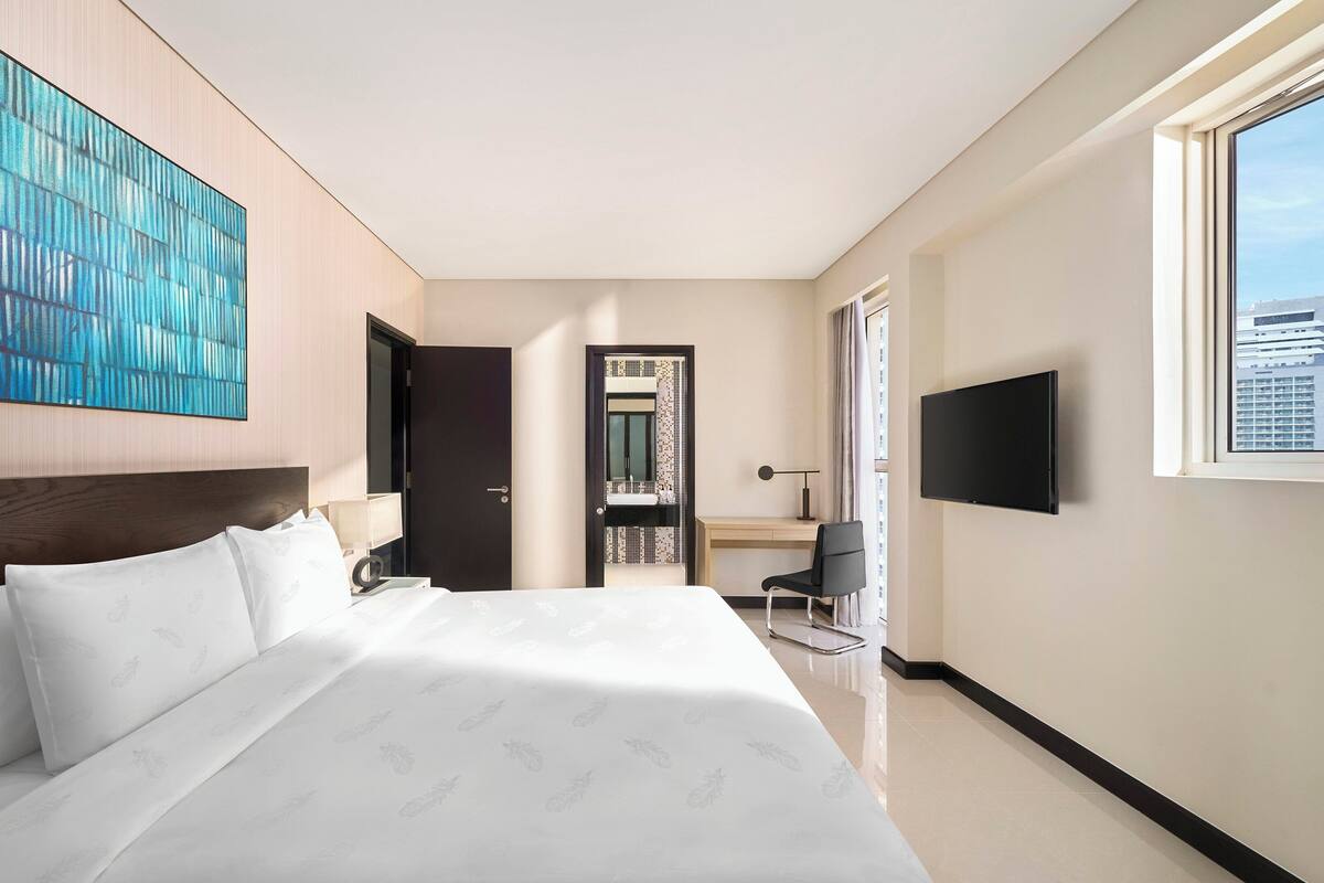 Une chambre d’hôtel moderne dotée d’un grand lit, d’un bureau avec une chaise, d’une télévision et offrant une vue sur la ville.