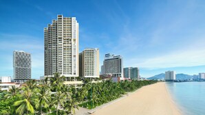 Um hotel na praia com vários edifícios altos, palmeiras e um céu claro.
