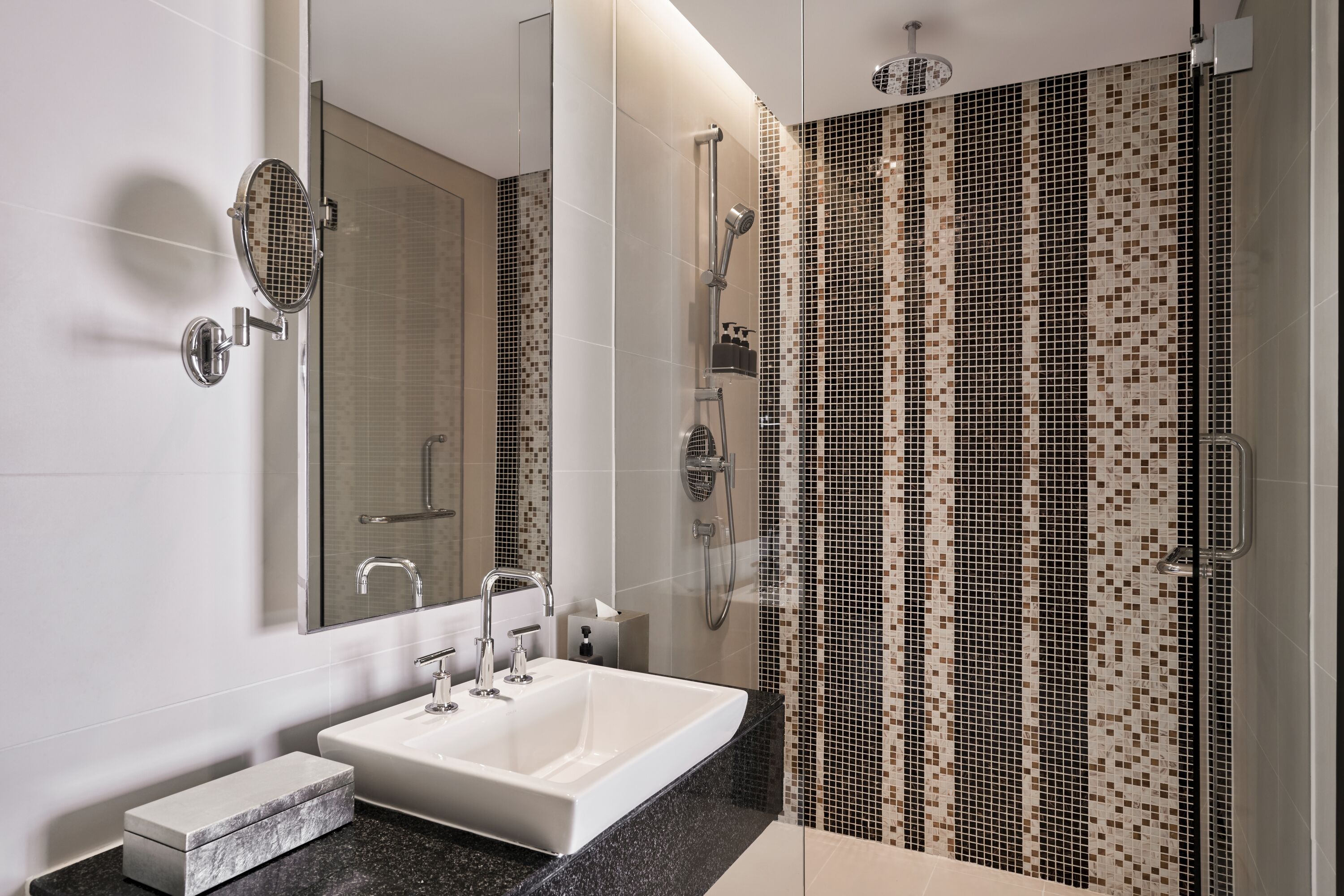 A modern bathroom with a large mirror, a white sink, and a shower area.