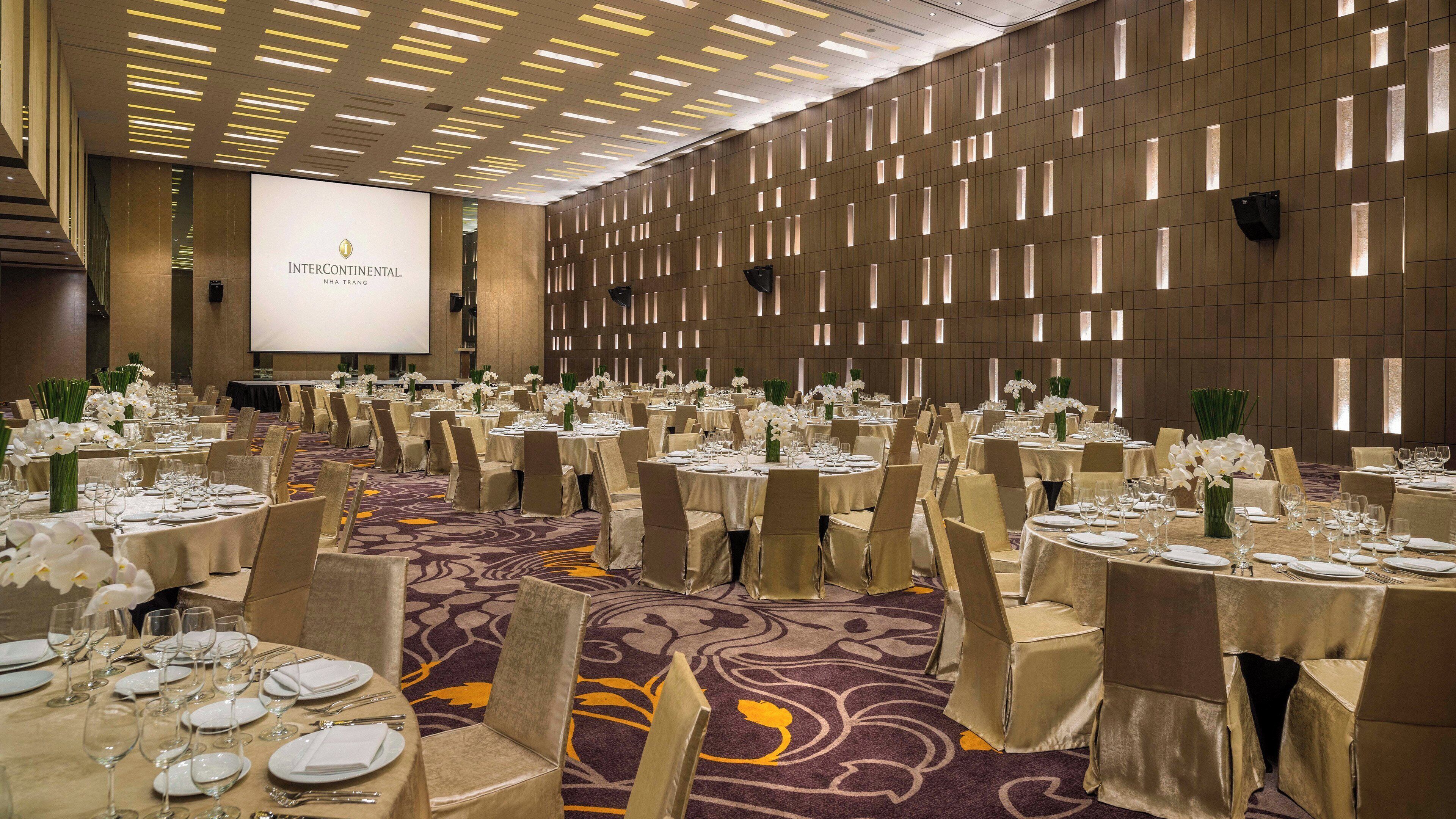 A conference room with multiple round tables set for a formal event, featuring a large screen and a decorative wall with vertical lighting.
