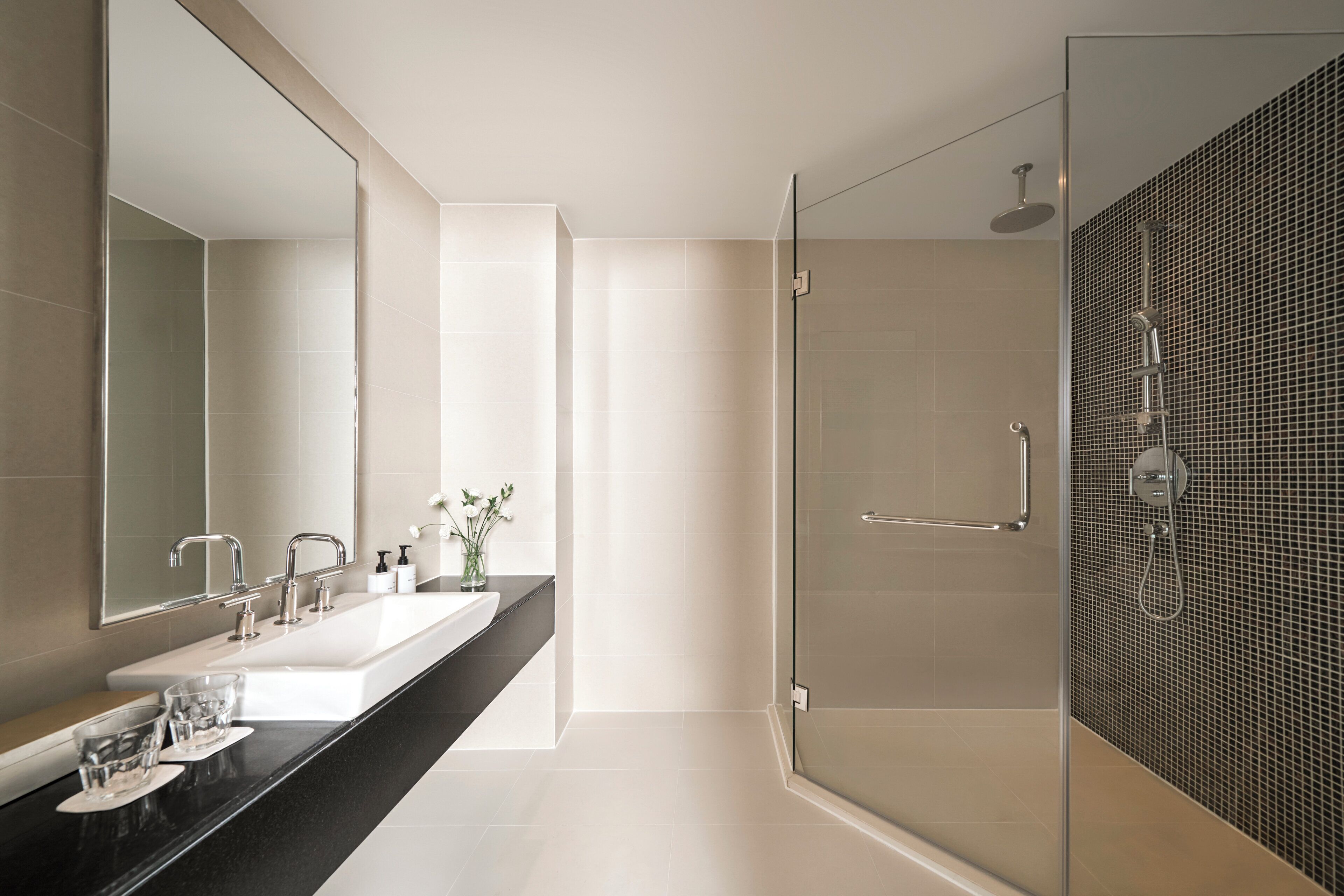 A modern bathroom with a glass-enclosed shower, a large mirror, and a black countertop with a sink and two faucets.