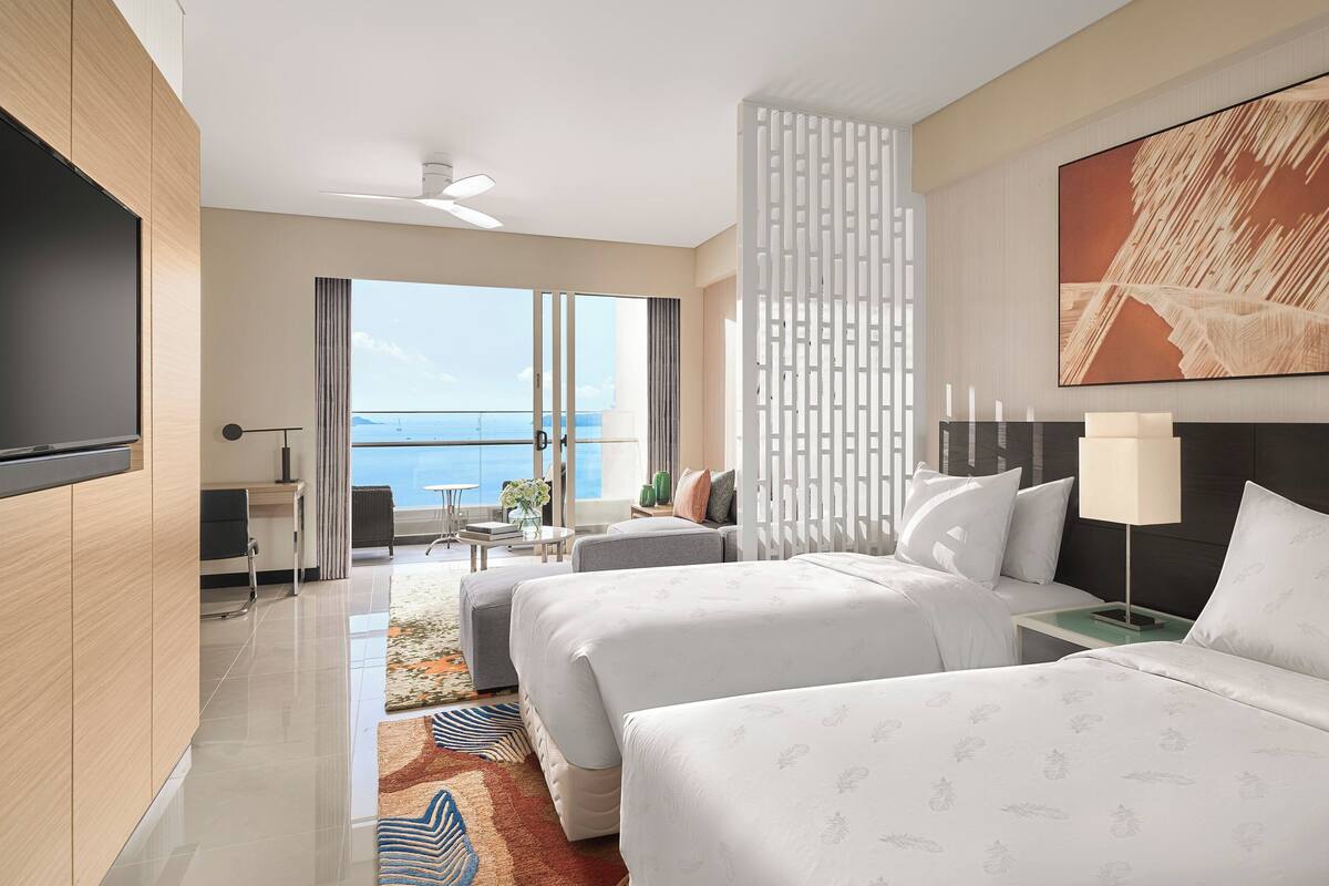 Une chambre d’hôtel avec deux lits, une télévision, un balcon donnant sur la mer et un tableau au mur.