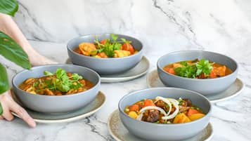 Four bowls of soup on ceramic plates, arranged on a marble surface.