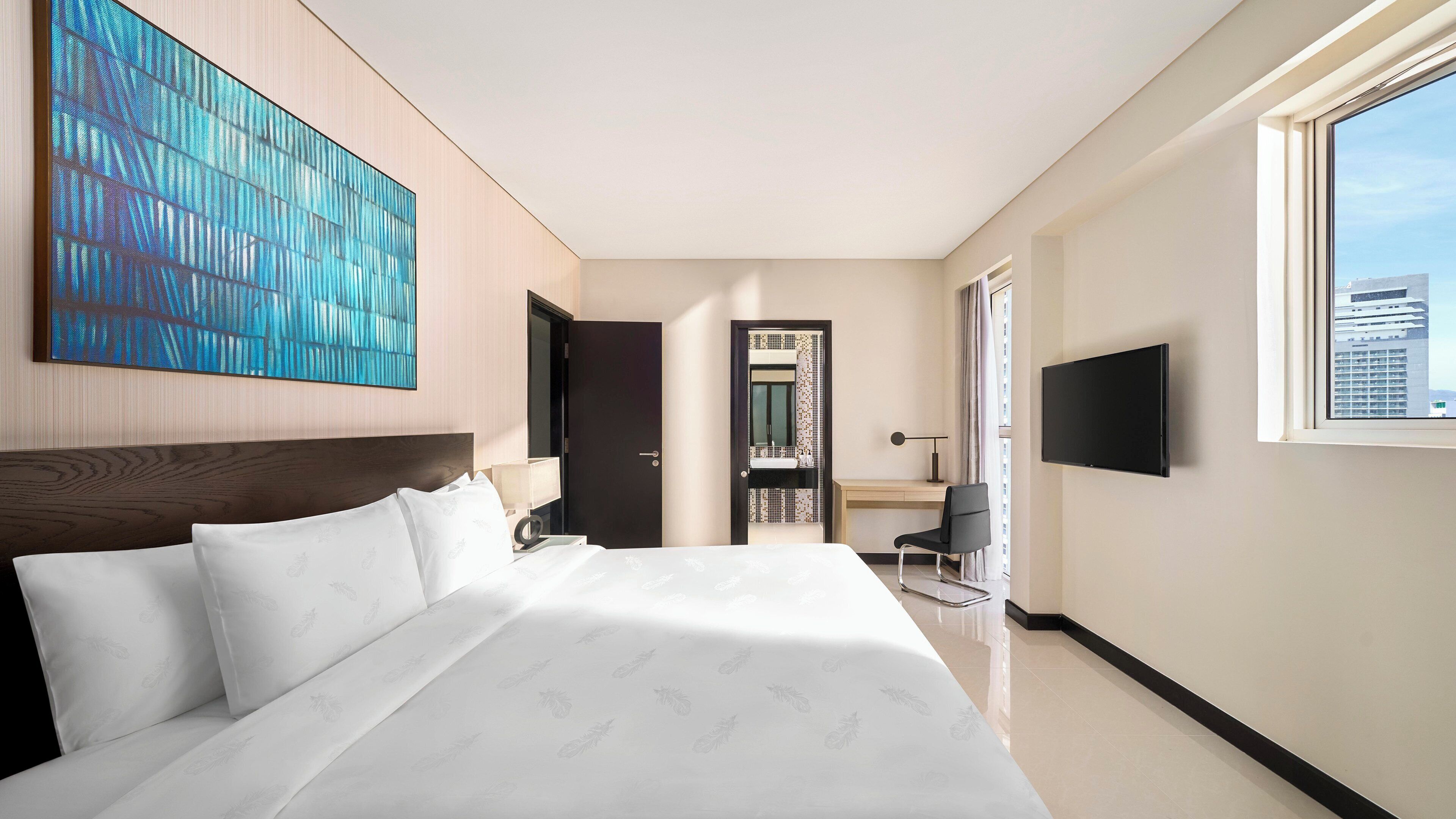 A modern hotel room with a large bed, a desk with a chair, a TV, and a city view.