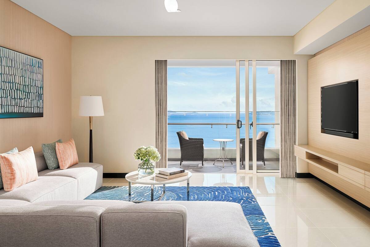 Une chambre d’hôtel moderne avec balcon, canapé, télévision et vue sur la mer.