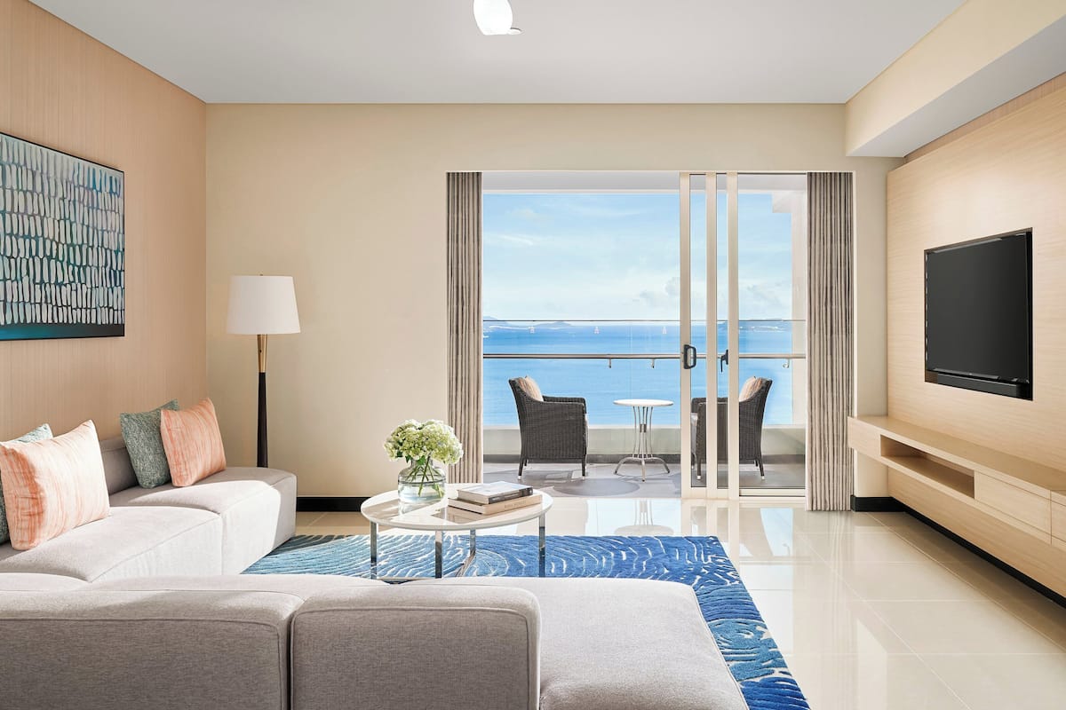 Une chambre d’hôtel moderne avec balcon, canapé, télévision et vue sur la mer.