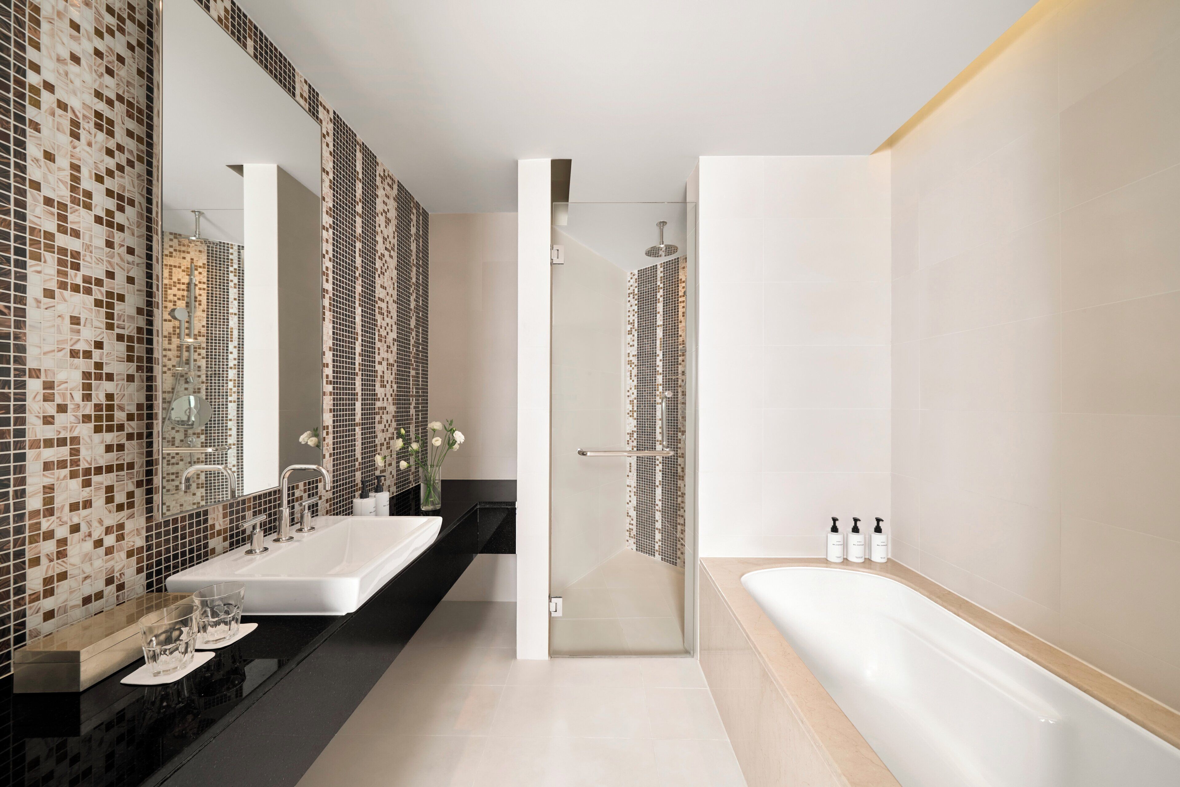 A modern bathroom with a large mirror, two sinks, a bathtub, and a shower area.