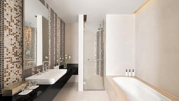 A modern bathroom with a large mirror, two sinks, a bathtub, and a shower area.