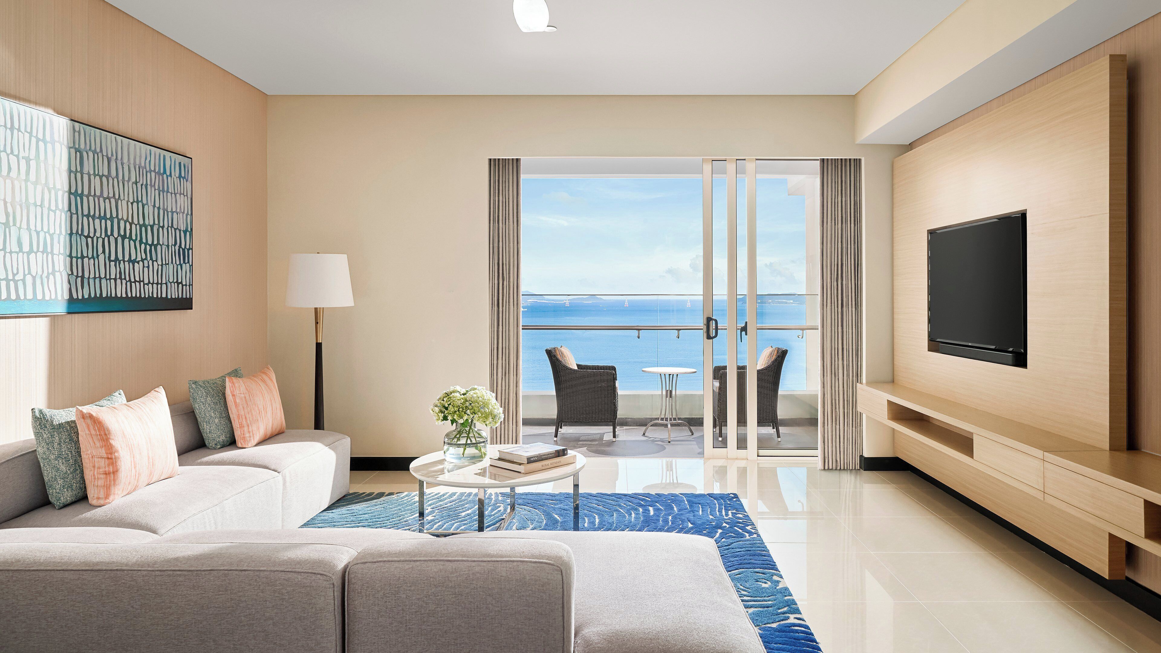 Habitació d'hotel moderna amb balcó, un sofà, televisió i vista al mar.