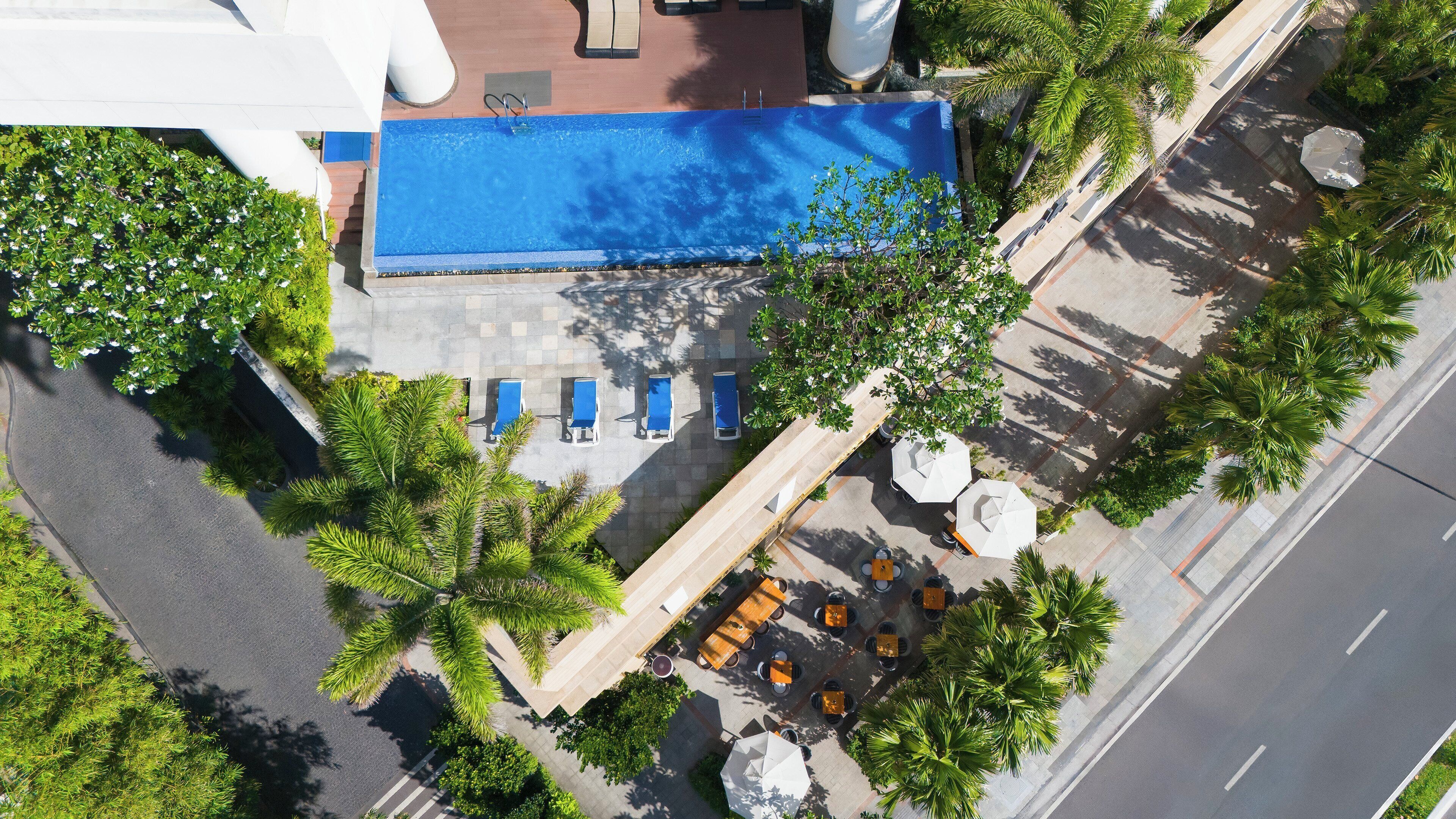 An aerial view of a hotel with a swimming pool, outdoor seating area, and palm trees.
